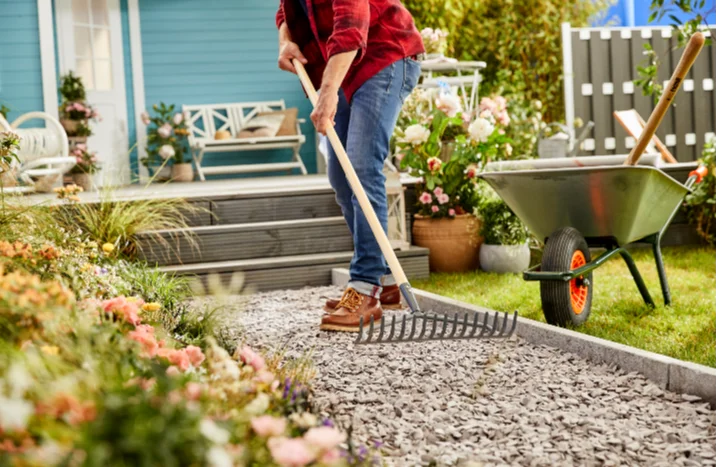 Person harkt Kiesweg im Garten