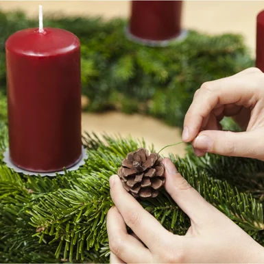 Person dekoriert Adventskranz mit Tannenzapfen