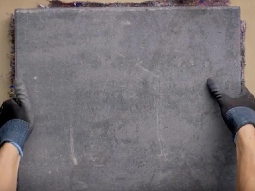 Zwei Hände in Arbeitshandschuhen halten eine Betonplatte hoch.