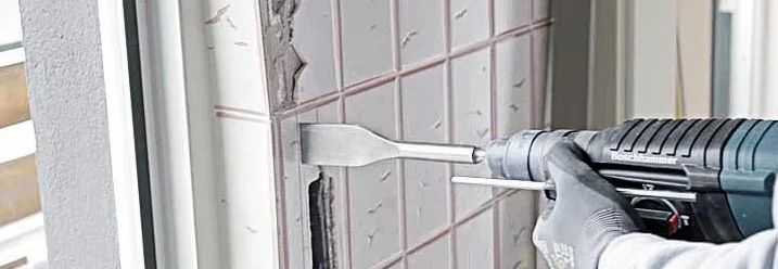Person entfernt Fliesen mit Meißelhammer