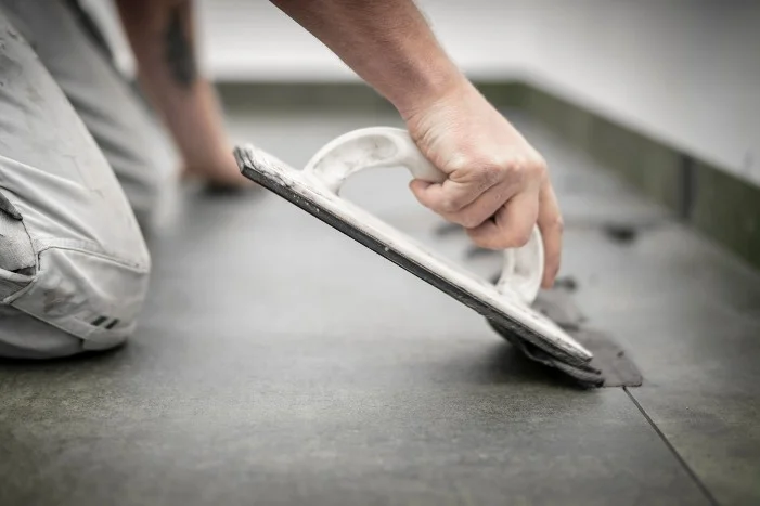 Person verfugt Fliesen mit Kelle