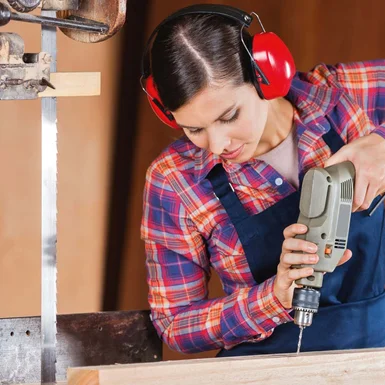 Person mit Gehörschutz bohrt in Holz