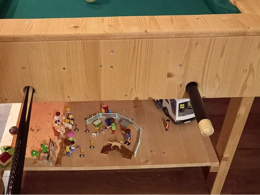 Spielzeugfiguren auf einer Holzplatte unter einem Billardtisch