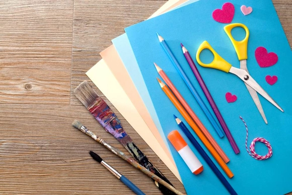 Bastelutensilien wie Buntstifte, Pinsel und Schere auf einem Holztisch.