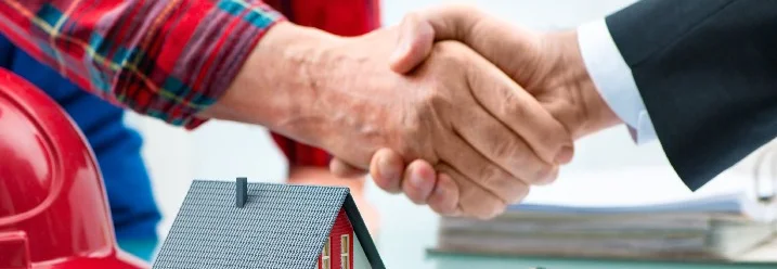 Zwei Personen geben sich die Hand über einem kleinen Musterhaus