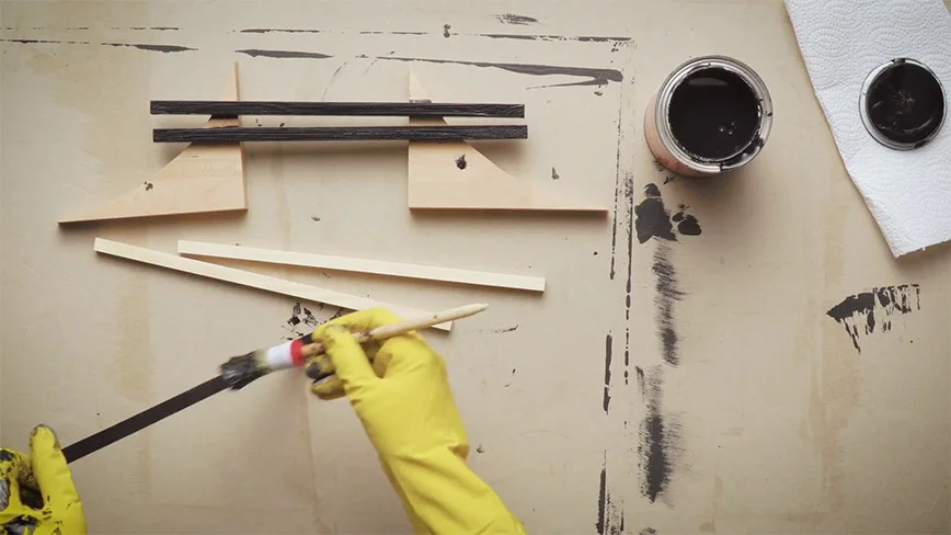 Person streicht Holzlatten schwarz an