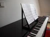 Ein schwarzes Digitalpiano mit Notenblättern auf einem Notenständer.