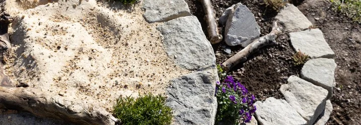 Eine runde Trockenmauer mit Sand und Pflanzen.