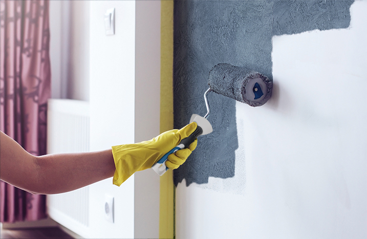 Eine Frau mit gelbem Malerhandschuh streicht eine Wand in grau.