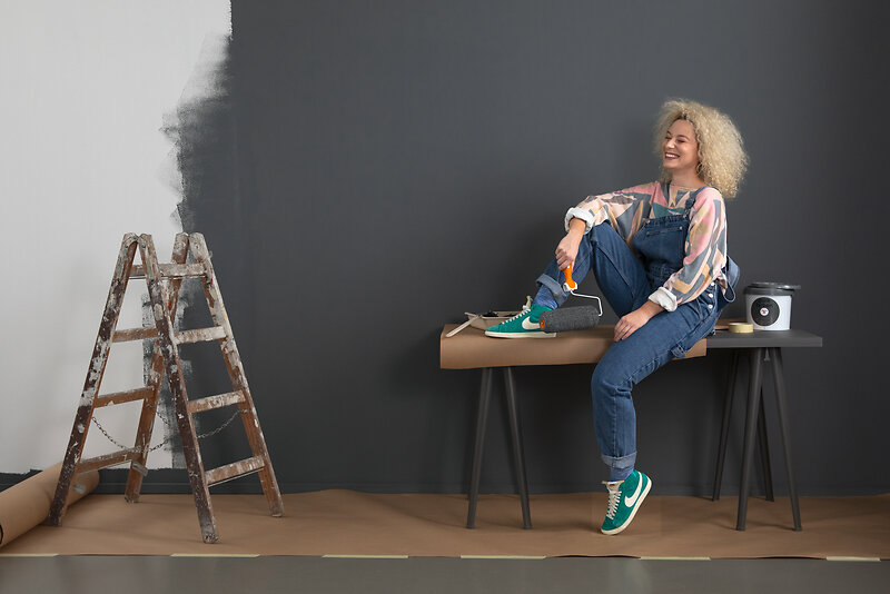 Person sitzt auf einem Tisch und hält eine Farbrolle.