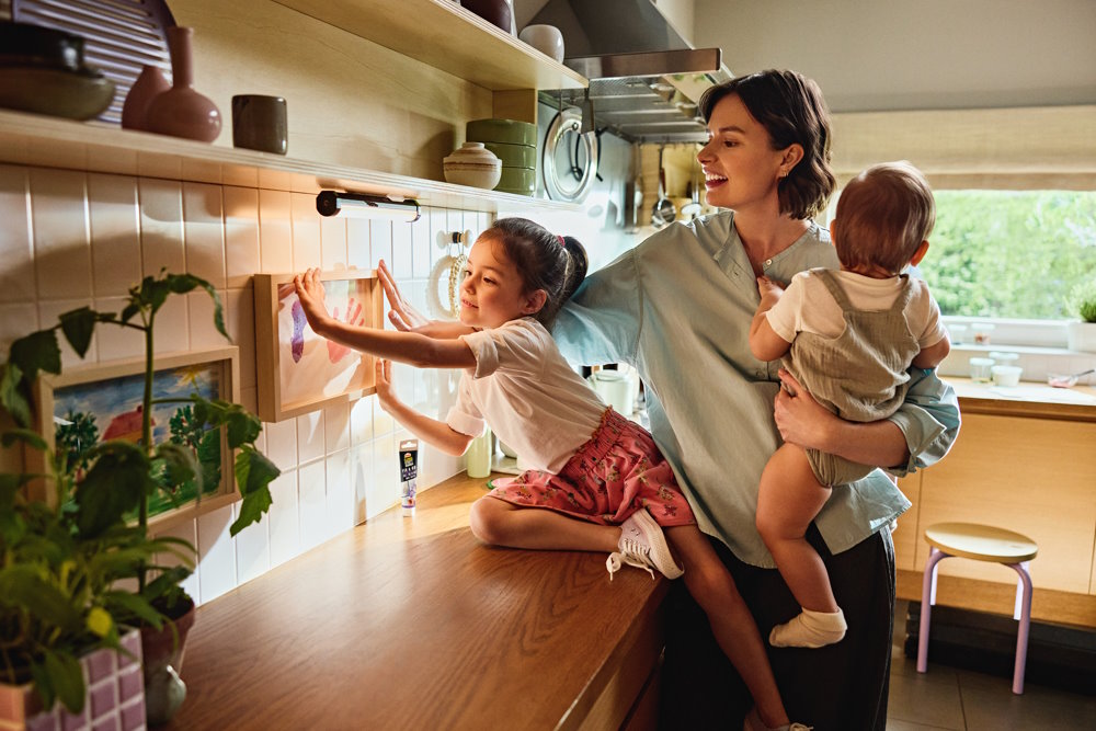 Kind hängt Bild mit Klebstoff an die Wand