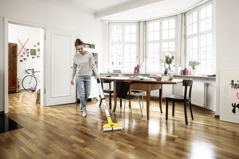 Person reinigt Holzboden mit Wischer