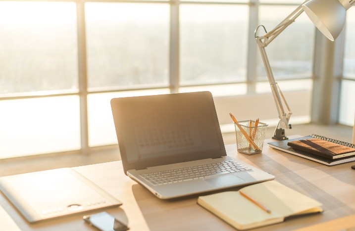 Sonne fällt durch große Fenster auf einen Schreibtisch mit Laptop