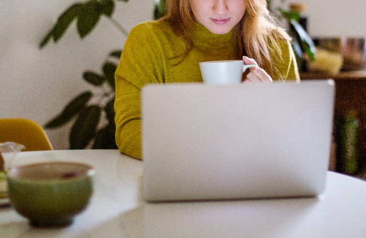 Frau sitzt mit Kaffee vor einem Laptop
