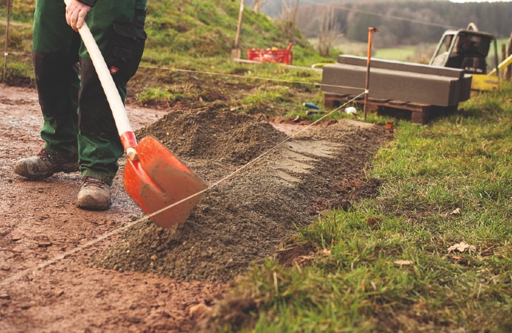 Ein Handwerker verteilt eine Schicht aus Kies und Sand für ein Fundament.