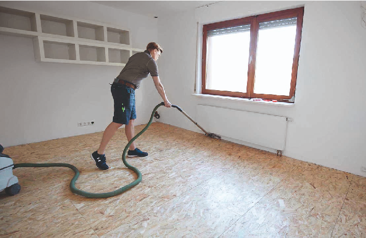 Eine Handwerkerin saugt den Boden in einem Zimmer.