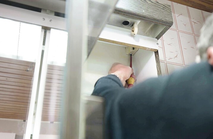 Schraubenzieher löst eine Schraube am geöffneten Spiegelschrank.