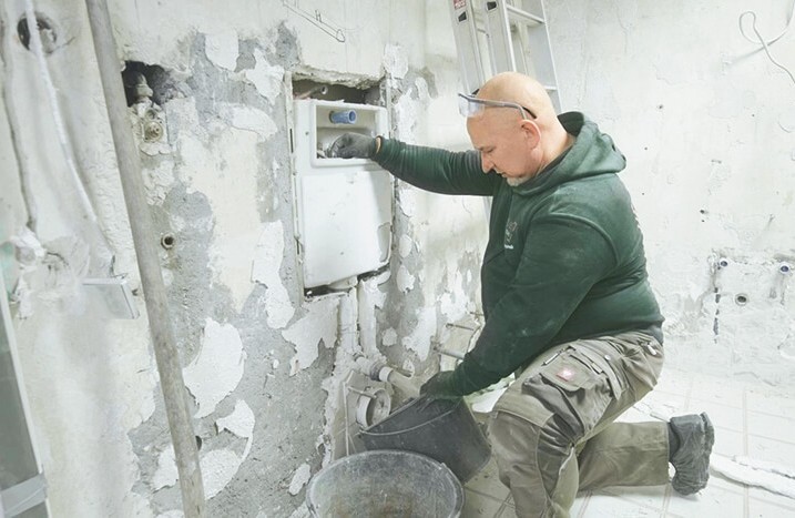 Mann lässt Wasser aus dem Unterputz-Spülkasten in Eimer ablaufen.