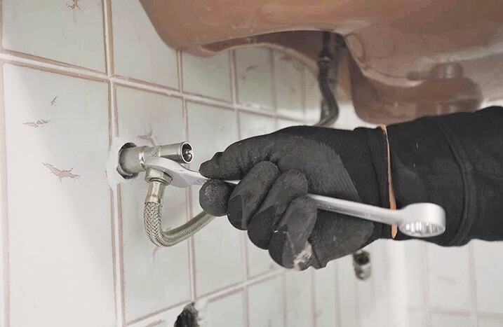 Mit einem Zangenschlüssel werden die Verbindungen zwischen den Eckventilen unter dem Waschbecken gelöst.