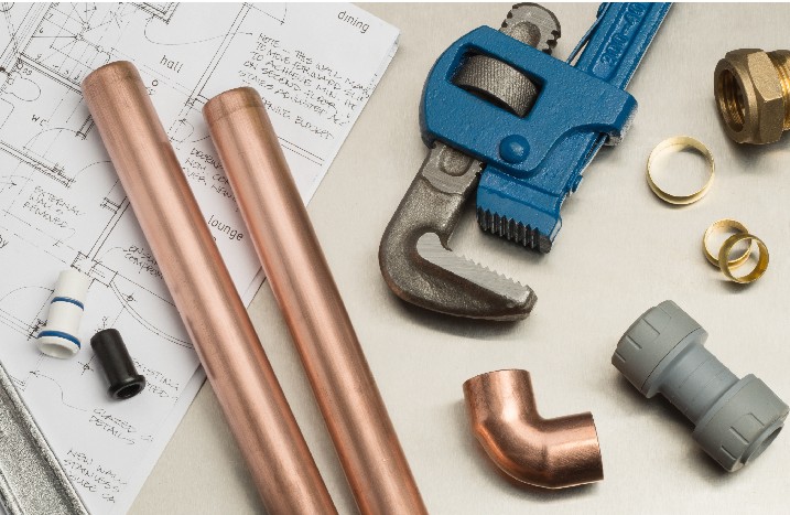 Diverse Materialen und Werkzeuge zum Verlegen von Rohren neben einem Bauplan.