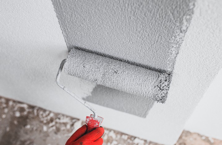 Nahaufnahme einer Walze mit grauer Farbe, die auf einer weißen Wand abgerollt wird.
