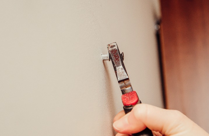 Nahaufnahme einer Schraube im Dübel, die mit einer Zange aus der Wand gezogen wird.