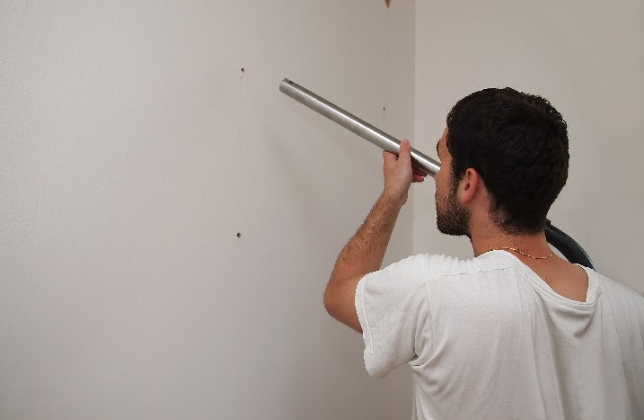 Ein Mann saugt ein Bohrloch in einer Wand aus. 