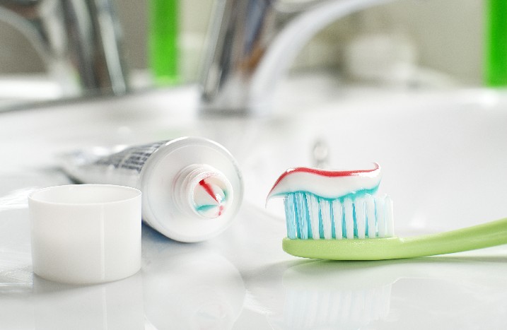 Eine Tube mit bunter Zahnpasta liegt neben einer Zahnbürste auf dem Waschbeckenrand.