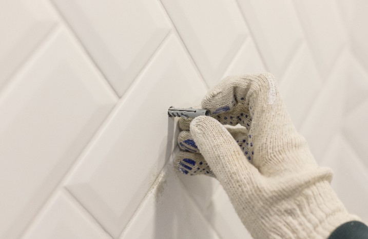 Hand mit Handschuh entfernt einen Dübel auf gefliester Wand.