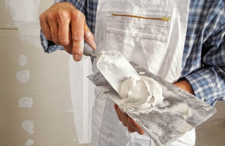 Ein Handwerker in Arbeitsklamotten bereitet Spachtelmasse auf einer Kelle vor.