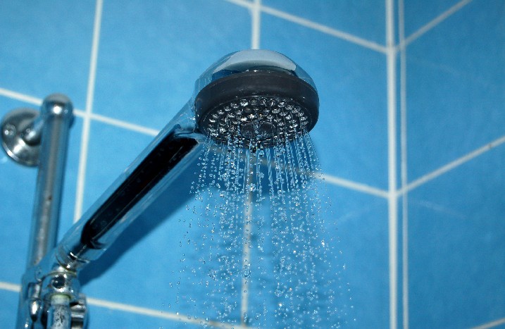 Eine laufende Dusche in einem hellblau gefliesten Badezimmer.