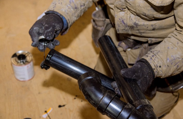 Mann trägt Kleber auf Kunststoffrohr auf