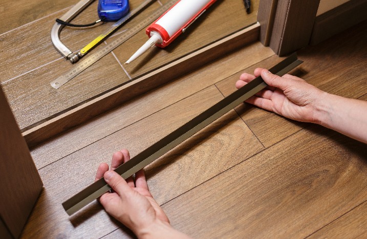Bauarbeiter, der ein Metallprofil mit Klebstoff an der Türschwelle befestigt.