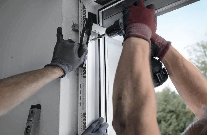 Gemeinsam schrauben zwei Handwerker die Terrassentür in die Wand.
