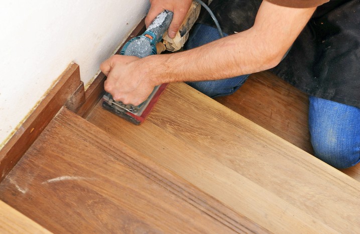 Mann bearbeitet Holztreppe mit Schwingschleifer