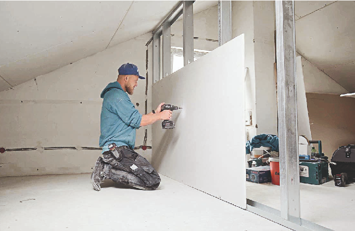 Ein Handwerker befestigt Gipsplatten am Ständerwerk.
