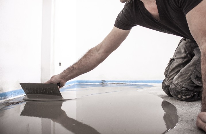 Handwerker verteilt Dichtmasse auf dem Fußboden.