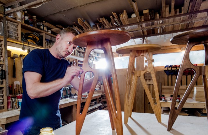 Mann mit drei aufgearbeiteten Holzhockern