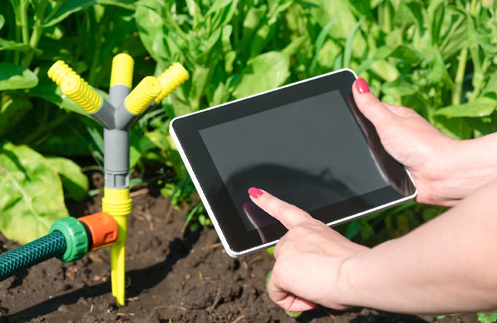 Eine Frau bedient ihr Tablet im Garten vor der Sprenkleranlage.