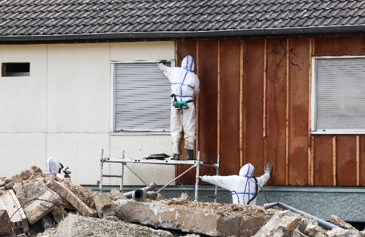 Personen in Ganzkörperschutzanzügen entfernen Asbest von einer Fassade.