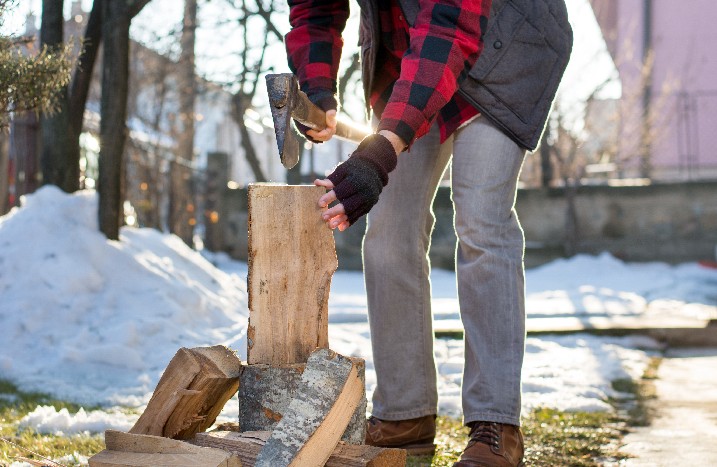 Ein Mann im winterlichen Garten setzt Axt zum Holz hacken an.