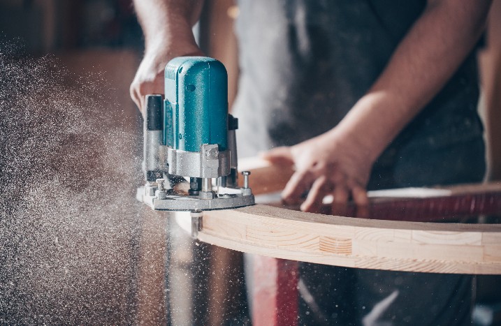 Mann feilt Holzstück mit Elektrowerkzeug