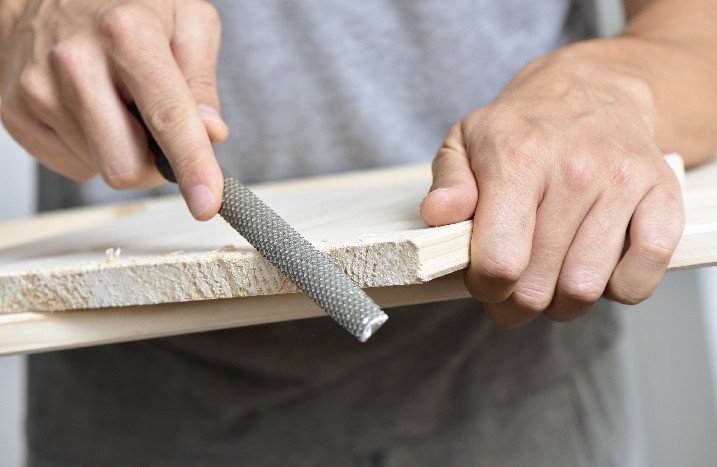 Mann raspelt Holzkante mit Handwerkzeug