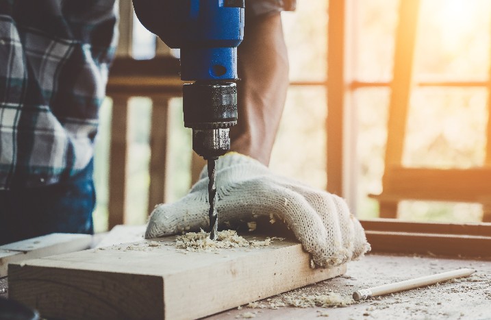 Mann mit Handschuh bohrt in Holzbrett