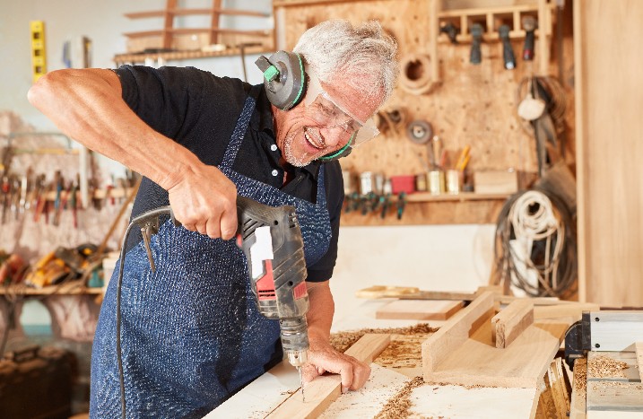 Mann mit Schutzbrille und Ohrschützern bohrt in Holzbrett