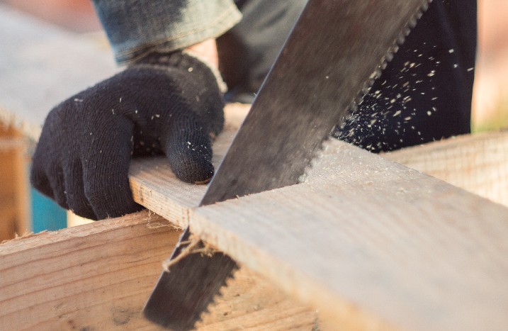 Mann mit Schutzhandschuhen sägt Holzstück wird mit Handsäge