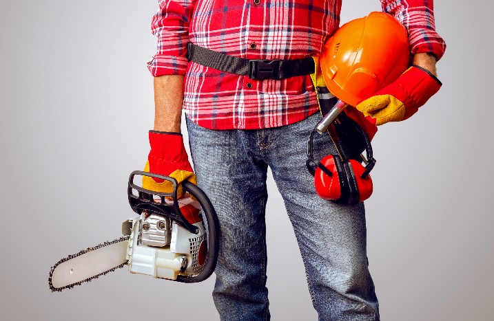 Mann mit Kettensäge, Schutzhelm und Ohrenschutz in der Hand