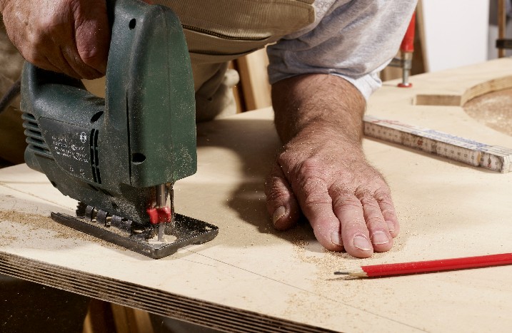 Mann sägt Holz mit Stichsäge.
