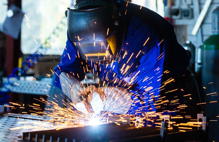 Schweißer einer Werkstatt schweißt Metall mit Schweißschutzhelm und Handschuhen
