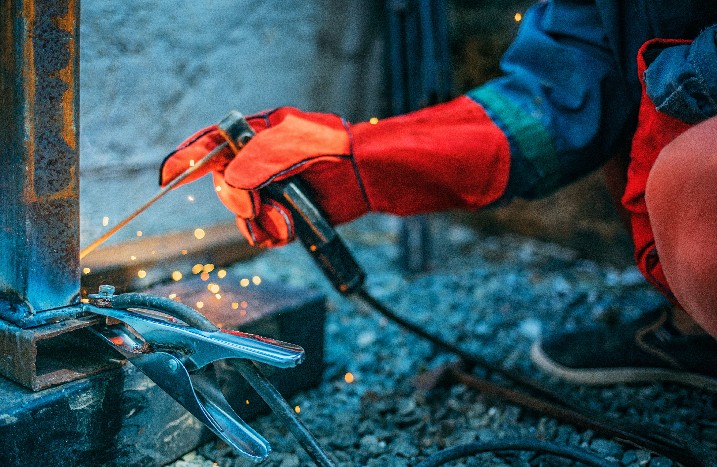 Schweißer schweißt ein Metallrohr mit Elektroschweißen und hält eine Elektrode in den Händen